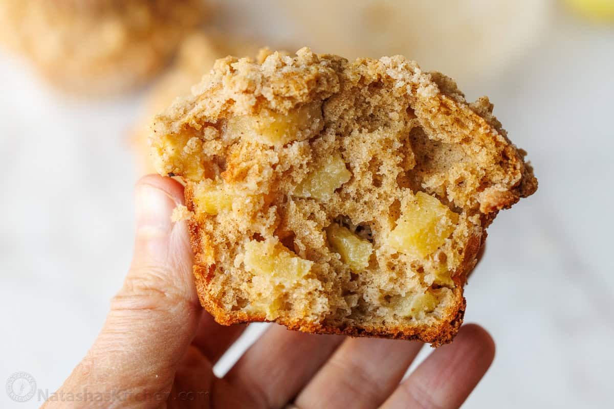 a hand holding half of a soft apple muffin with chunks of apples inside.