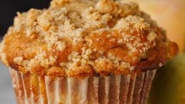 Apple muffin with crumb topping on a table with a white muffin wrapper