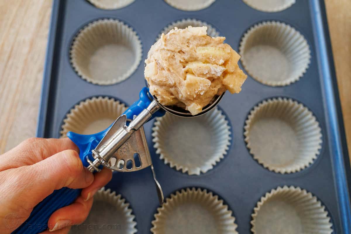Ice cream scoop adding batter to a muffin tin with muffin liners