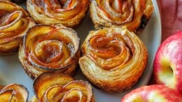 Apple roses lined up on a plate with two apples