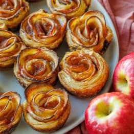 Apple roses lined up on a plate with two apples