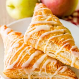 Two apple turnovers on a plate with apples in background