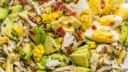 Avocado Chicken Salad in a white bowl with hardboiled eggs and bacon bits on top