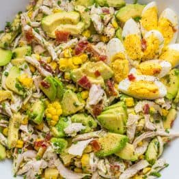 Avocado Chicken Salad in a white bowl with hardboiled eggs and bacon bits on top