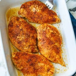 Baked chicken Breasts in white casserole dish with serving fork