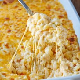 Scoop of Baked Mac N Cheese removed from a white dish with a metal spoon