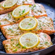fillets of baked salmon in a frying pan with lemon slices and garlic-parsley sauce