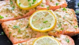 fillets of baked salmon in a frying pan topped with lemon slices and parsley