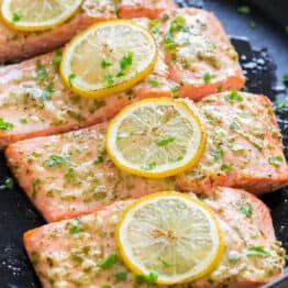 fillets of baked salmon in a frying pan topped with lemon slices and parsley
