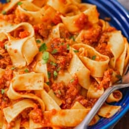 Pappardelle pasta with bolognese sauce in a blue bowl, with a fork.