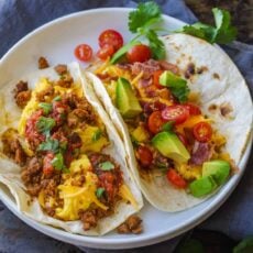 Two breakfast tacos filled with chorizo on a white plate.