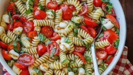 Caprese pasta salad recipe in a white bowl with a spoon for serving.
