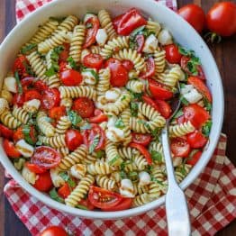 Caprese pasta salad recipe in a white bowl with a spoon for serving.