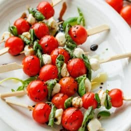 Caprese skewers recipe with tomatoes, basil, mozzarella pearls and balsamic glaze on a white plate