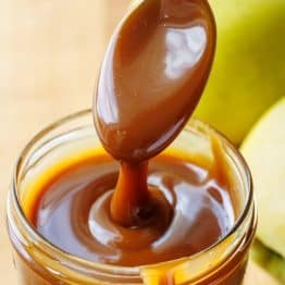 Spoon drizzling dark brown caramel sauce from scratch into a mason jar