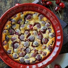 French Cherry clafoutis dessert in a red dish with fresh cherries