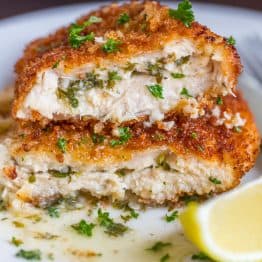 Chicken Kiev recipe cut in half on a white plate with lemon wedge and parsley garnish