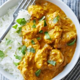 Chicken Korma and white rice in a dish with a fork, garnished with chopped cilantro
