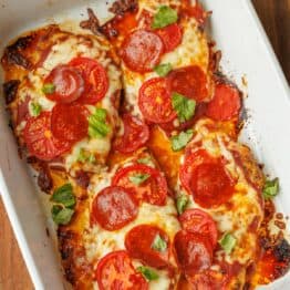 Pizza Chicken baked in a rectangle baking pan. 4 chicken breasts covered in pizza sauce, mozzarella cheese, pepperoni, and chopped basil