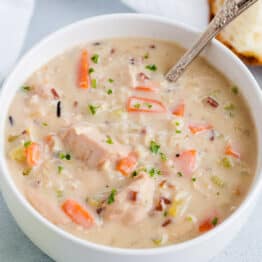 A bowl of chicken and wild rice soup in a bowl with a spoon and slice of bread
