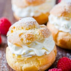 Cream puffs served dusted with powdered sugar surrounded by raspberries