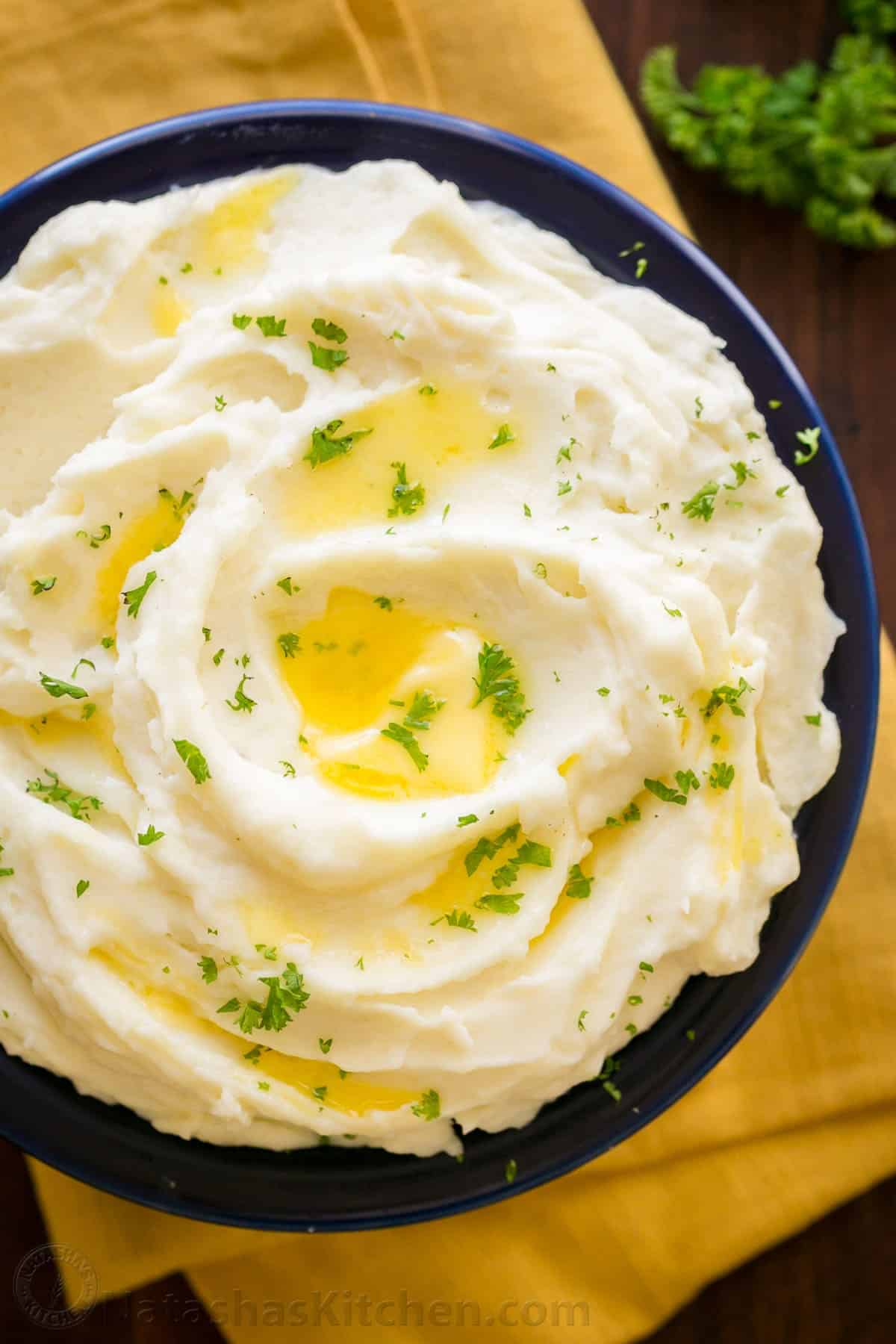 The creamiest whipped mashed potatoes recipe drizzled with butter and garnished with parsley