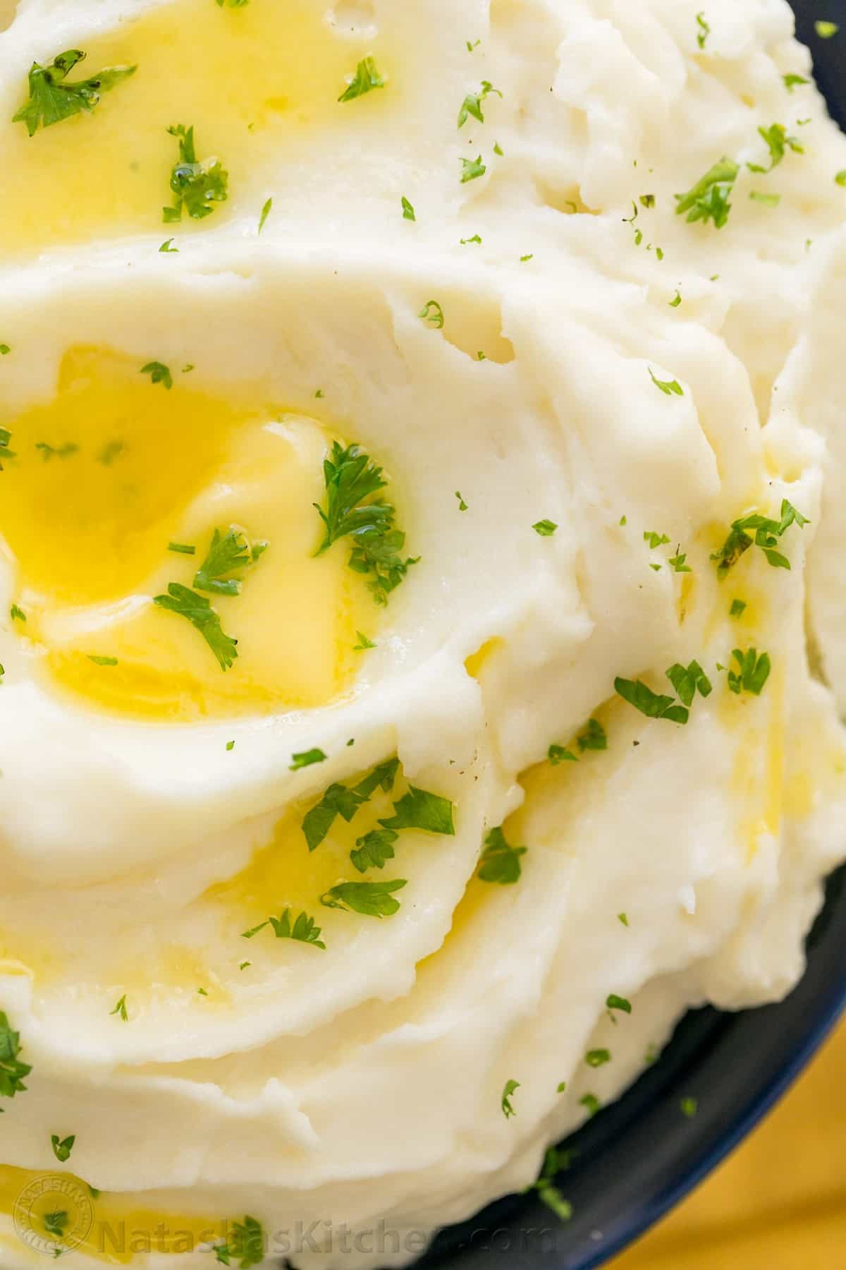 Creamy mashed potatoes recipe drizzled with butter and sprinkled with parsley