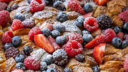 Dusting powdered sugar over croissant French Toast Casserole in a white dish