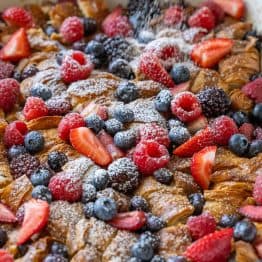 Dusting powdered sugar over croissant French Toast Casserole in a white dish