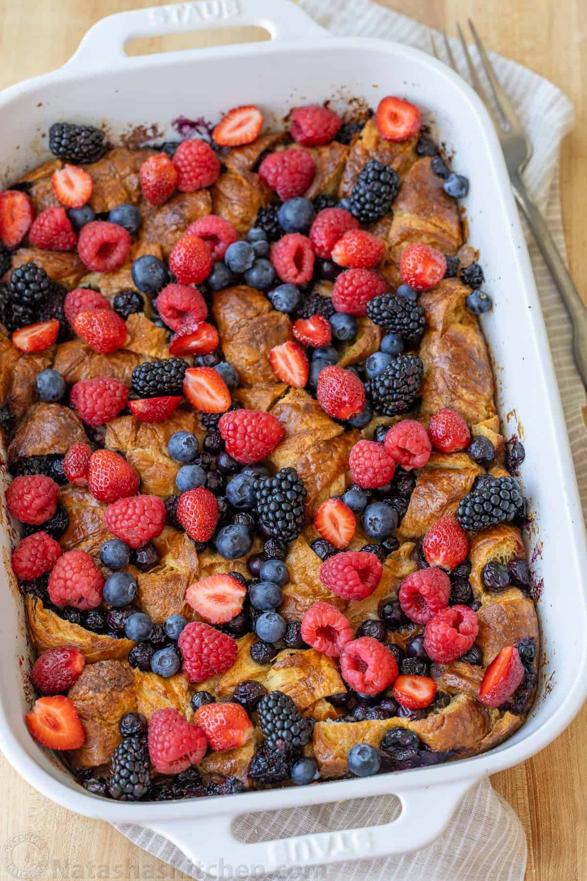 Berries and cut strawberries scattered over Croissant French Toast Bake in a white dish