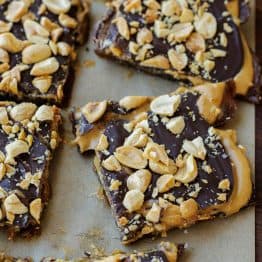 Date Snickers cut into individual pieces, made with a base of medjool dates, topped with creamy peanut butter, and covered in a layer of melted chocolate and topped with peanuts.