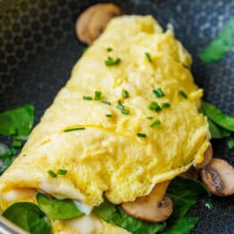 Omelette cooked in a skillet with spinach and mushrooms