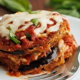 Breaded eggplant Parmesan layered with marinara sauce and mozzarella cheese, and garnished with fresh basil served on a plate with a fork