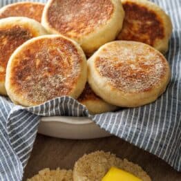 Butter spread on homemade english muffin with bowl of toasted crumpets
