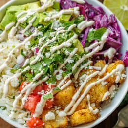 Easy Fish Taco Bowls using seasoned fish, cabbage, cilantro lime rice, cilantro, tomatoes and Fish Taco Sauce