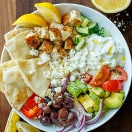 Chopped Greek Chicken Bowl ingredients in a white bowl with lemon wedges and pita bread