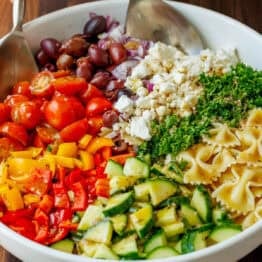 Greek Pasta Salad ingredients being tossed in a white serving dish