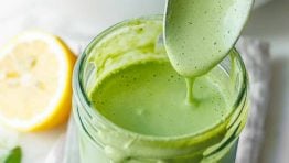 A spoon serving Green Goddess salad dressing from a mason jar onto a mixed green salad