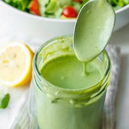 A spoon serving Green Goddess salad dressing from a mason jar onto a mixed green salad