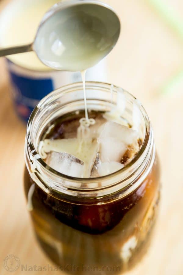 A mason jar with iced coffee and condensed milk is being added to it 