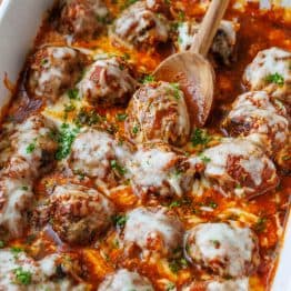 Serving meatball Parmesan using a wooden spoon from a white casserole dish