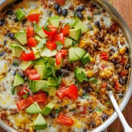 Mexican Ground Beef and Rice Skillet garnished with fresh diced tomatoes, avocado, and cilantro. Ready to serve with a spoon.