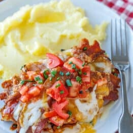 Monterey Chicken topped with melted Monterey jack cheese, tomatoes, crispy bacon, and chives. Served with mashed potatoes on a plate.