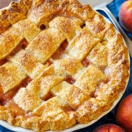 Peaches surrounding a homemade peach pie with browned crust and pie server