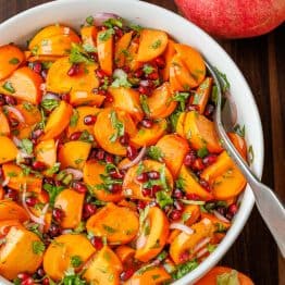Persimmon pomegranate salad in a white bowl with serving spoon.