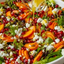 pouring dressing from a glass jar onto the persimmon salad