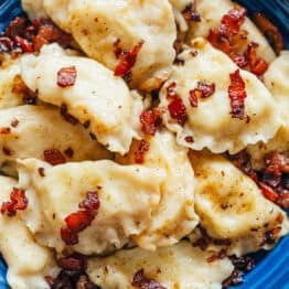 Cooked pierogies on a blue plate with bacon
