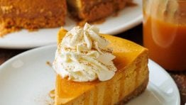 Pumpkin Cheesecake cut into pieces with one slice on a plate with caramel sauce drizzled on top