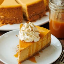 Pumpkin Cheesecake cut into pieces with one slice on a plate with caramel sauce drizzled on top