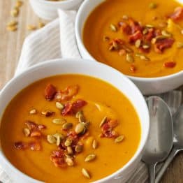 two bowls of pumpkin soup in white bowls with pumpkin seeds and bacon